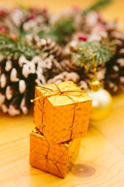 Small golden gift boxes stacked on a wooden surface, set against a blurred background of a festive Christmas wreath. clipart