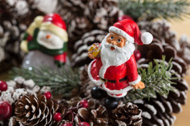 Kırmızı ve beyaz takım elbiseli küçük bir Noel Baba heykeli yeşil bir çuval tutuyor, bulanık bir arka plan üzerine kurulmuş. Bu şenlikli süs Noel ruhunu yansıtıyor..