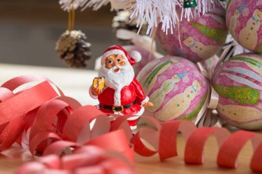 A small figurine of Santa Claus in a red and white suit holding a green sack, set against a blurred background. This festive ornament captures the spirit of Christmas. clipart