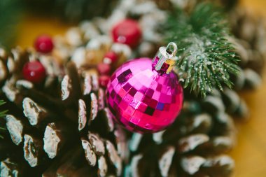 Christmas Decoration. Holiday wreath adorned with snow-dusted pine cones, evergreen branches, red berries, and shiny pink Christmas ornament clipart