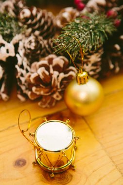 Small gold drum ornament and a gift box with a shiny, metallic wrapping placed on a wooden surface. The festive decorations capture the essence of Christmas and New Year celebrations, creating a warm and joyful holiday atmosphere. clipart