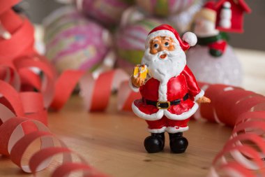 Kırmızı ve beyaz takım elbiseli küçük bir Noel Baba heykeli yeşil bir çuval tutuyor, bulanık bir arka plan üzerine kurulmuş. Bu şenlikli süs Noel ruhunu yansıtıyor..