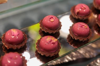 Kremalı ve süpriz çilek reçelli zarif kremalı pastalar, pürüzsüz pembe bir jöle ile kaplanmış ve dondurulmuş ahududu parçalarıyla kıtır bir bisküvi tabanı üzerine serpilmiş.