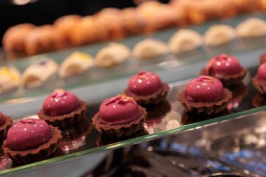 Kremalı ve süpriz çilek reçelli zarif kremalı pastalar, pürüzsüz pembe bir jöle ile kaplanmış ve dondurulmuş ahududu parçalarıyla kıtır bir bisküvi tabanı üzerine serpilmiş.