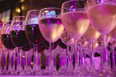 Beyaz bir masa örtüsü üzerine kurulmuş kırmızı ve beyaz şaraplarla dolu güzel bir şarap kadehi koleksiyonu. Resim, partiler, düğünler veya şarap tatma gibi etkinlikler için mükemmel bir sahne yakalıyor.