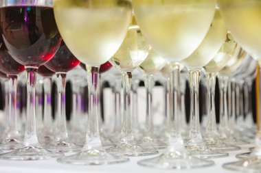 Beyaz bir masa örtüsü üzerine kurulmuş kırmızı ve beyaz şaraplarla dolu güzel bir şarap kadehi koleksiyonu. Resim, partiler, düğünler veya şarap tatma gibi etkinlikler için mükemmel bir sahne yakalıyor.