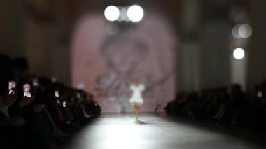 Moda pisti bulanık. Elbise giymiş bir manken ışıktaki yeni kıyafet koleksiyonu sırasında podyumda yürür..