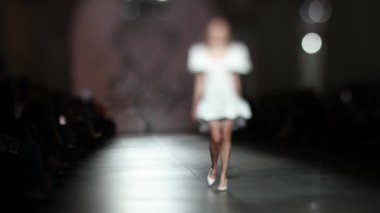 Moda pisti bulanık. Elbise giymiş bir manken ışıktaki yeni kıyafet koleksiyonu sırasında podyumda yürür..