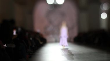 Moda pisti bulanık. Elbise giymiş bir manken ışıktaki yeni kıyafet koleksiyonu sırasında podyumda yürür..