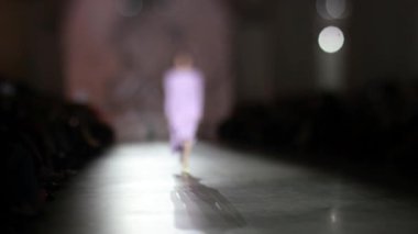 Moda pisti bulanık. Elbise giymiş bir manken ışıktaki yeni kıyafet koleksiyonu sırasında podyumda yürür..