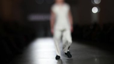 Fiziksel engelli erkek manken defilede podyumda yürüyor. Moda podyumu etkinliği yeni kıyafet koleksiyonunu gösteriyor. Yavaş çekim.