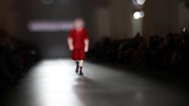 Fiziksel engelli erkek manken defilede podyumda yürüyor. Moda podyumu etkinliği yeni kıyafet koleksiyonunu gösteriyor. Yavaş çekim.