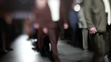 Fiziksel engelli erkek manken defilede podyumda yürüyor. Moda podyumu etkinliği yeni kıyafet koleksiyonunu gösteriyor. Yavaş çekim.