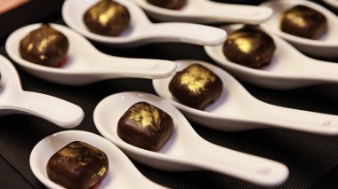 Elegant gourmet chocolate truffles with a touch of edible gold dust, carefully presented on white porcelain spoons.