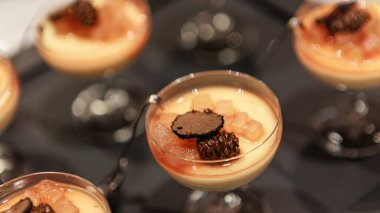 Elegant gourmet dessert served in delicate glassware, featuring a creamy panna cotta base topped with caramelized pear and thinly sliced black truffle