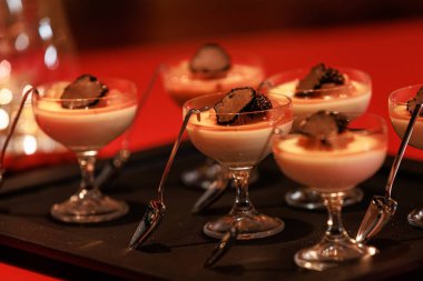 Elegant gourmet dessert served in delicate glassware, featuring a creamy panna cotta base topped with caramelized pear and thinly sliced black truffle
