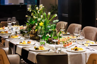 Lüks bir yemek masasında beyaz laleleri ve yemyeşil çiçekleri olan zarif bir süs, sofistike etkinlikler, düğünler ve güzel yemek dekorları için ideal..