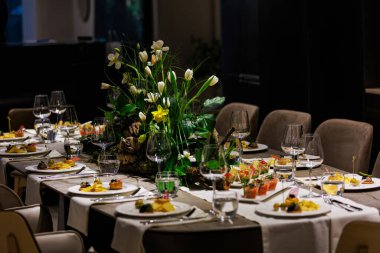 Lüks bir yemek masasında beyaz laleleri ve yemyeşil çiçekleri olan zarif bir süs, sofistike etkinlikler, düğünler ve güzel yemek dekorları için ideal..