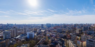 Geniş hava manzarası Kyiv 'in dinamik ufuk çizgisini açık mavi bir gökyüzü altında yakalıyor, modern yüksek binalar ve işlek bir şehir caddesinin yanında tarihi binaların canlı bir karışımını sunuyor.