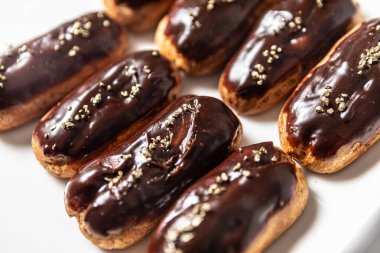 Beyaz bir tabakta düzgünce dizilmiş sekiz klasik eklem. Her pasta parlak bir çikolata jölesi içeriyor ve narin altın parçacıklarıyla süslenmiş.