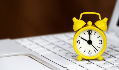 Beyaz dizüstü bilgisayarda sarı alarm saati. Yaz saati pankartı ya da arkaplan.