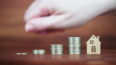 Bir el, madeni paraların ve evin arkasına para saçıyor. İpotek kredisi, gayrimenkul yatırımı veya ev satın alma, daire sahipliği kavramı. 