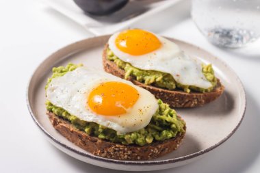 Avokado yumurtalı sandviç ve bir bardak su. Sağlıklı hafif kahvaltı konsepti. Avokado püresi ve kızarmış yumurta ile tam tahıllı tost.