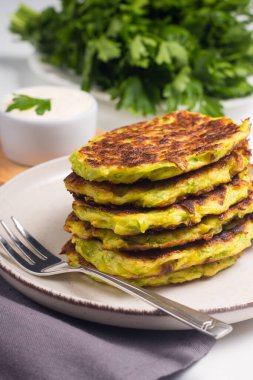 Vegetarian zucchini fritters or courgettes pancakes, served with fresh herbs and sour cream.