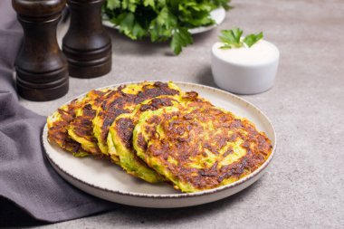 Vegetarian zucchini fritters or courgettes pancakes, served with fresh herbs and sour cream.