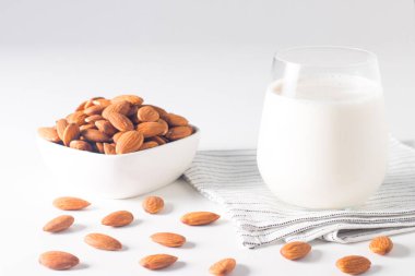 Bardakta organik badem sütü ve beyaz masada çiğ badem. 