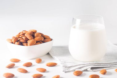 Bardakta organik badem sütü ve beyaz masada çiğ badem. 
