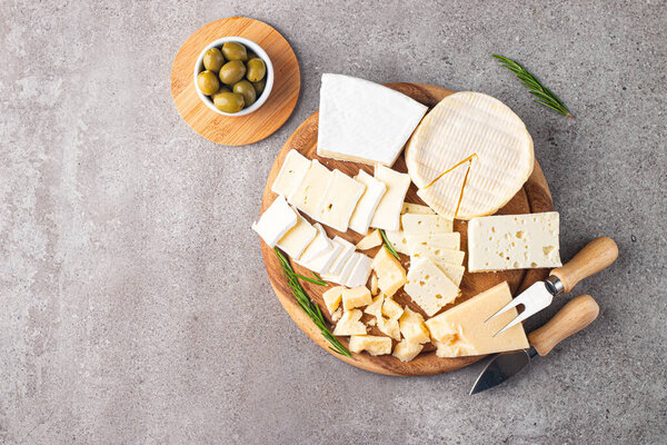 Wooden board with various cheese and olives. Brie. Camembert. Parmesan, feta, blue cheese. Italian, French cheese.