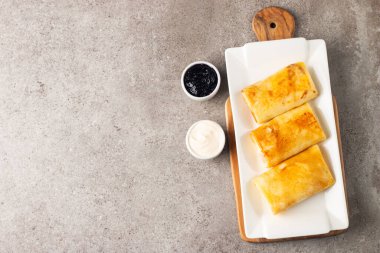 Süzme peynirle doldurulmuş ince krepler ekşi krema ve siyah frenk üzümü reçeli ile servis edilir. Fransız krepleri. 