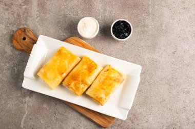 Süzme peynirle doldurulmuş ince krepler ekşi krema ve siyah frenk üzümü reçeli ile servis edilir. Fransız krepleri. 