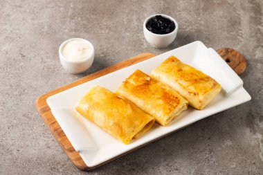 Süzme peynirle doldurulmuş ince krepler ekşi krema ve siyah frenk üzümü reçeli ile servis edilir. Fransız krepleri. 