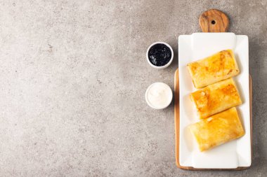 Süzme peynirle doldurulmuş ince krepler ekşi krema ve siyah frenk üzümü reçeli ile servis edilir. Fransız krepleri. 