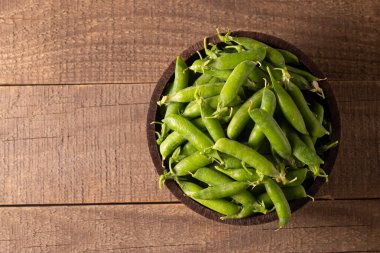 Tahta masadaki bir kasede taze bezelye ve kabuklar. Sebzeli sağlıklı yiyecek..  