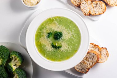 Sıcak ve rahatlatıcı kremalı brokoli çorbası bir kasede servis edilir, parmesan peyniri ve kızarmış ekmekle süslenir..