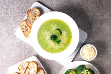 Sıcak ve rahatlatıcı kremalı brokoli çorbası bir kasede servis edilir, parmesan peyniri ve kızarmış ekmekle süslenir..