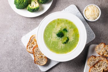 Sıcak ve rahatlatıcı kremalı brokoli çorbası bir kasede servis edilir, parmesan peyniri ve kızarmış ekmekle süslenir..