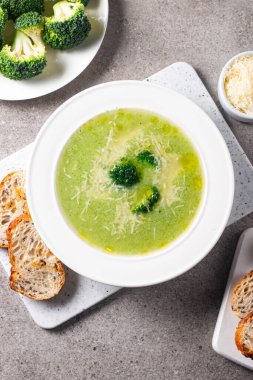 Sıcak ve rahatlatıcı kremalı brokoli çorbası bir kasede servis edilir, parmesan peyniri ve kızarmış ekmekle süslenir..