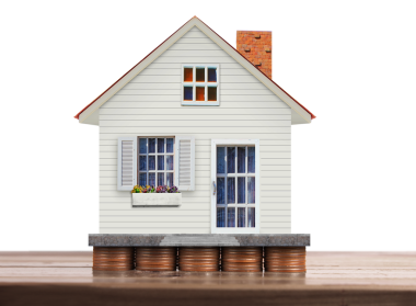 Madeni paraların üzerine tünemiş bir model ev, emlak yatırımıyla mali büyüme arasındaki bağlantıyı sembolize eder..