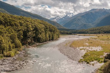 The Makarora river in the Otago region of New Zealand flowing towards Wanaka Lake with snow capped mountains in the distance