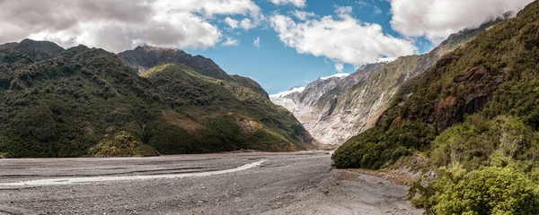 Panoramic view of the alluvial bed of the Waiho River flowing from the Franz Josef Glacier and snow capped mountains in New Zealand