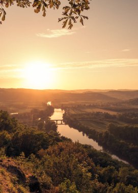Fransa 'nın Nouvelle-Aquitaine bölgesinde Dordogne nehri ve vadisi üzerindeki Cenac-et-Saint-Julien köprüsünde güneş batıyor.