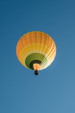 Rocamadour, Fransa - 24 Eylül 2023: Fransa 'da düzenlenen Montgolfiades de Rocamadour balon festivali sırasında sarı, turuncu ve yeşil bir sıcak hava balonu tepemizden geçer