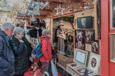 Sarlat-la-Caneda, Nouvelle-Aquitaine, Fransa - 16 Aralık 2023: Fransa 'nın Dordogne bölgesindeki Sarlat-la-Caneda Noel pazarında Viktorya dönemi kıyafetleri giymiş insanların resimlerini satan bir tezgah