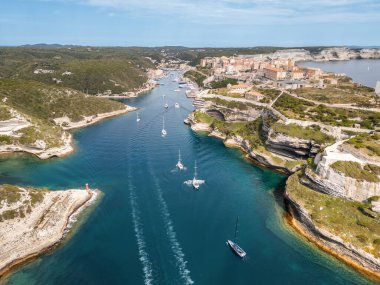 Limana giren ve Korsika 'daki duvarlı Bonifacio kalesini geçen yelkenli gemilerin hava görüntüsü.