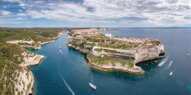 Kireçtaşı kayalıklarının panoramik hava manzarası, Korsika 'daki Bonifacio liman girişi ve kalesi, Sardunya kıyıları uzaklıktadır.
