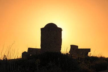 Korsika 'daki Bonifacio kayalıklarında terk edilmiş eski bir yel değirmeninin arkasında altın gün doğumu.
